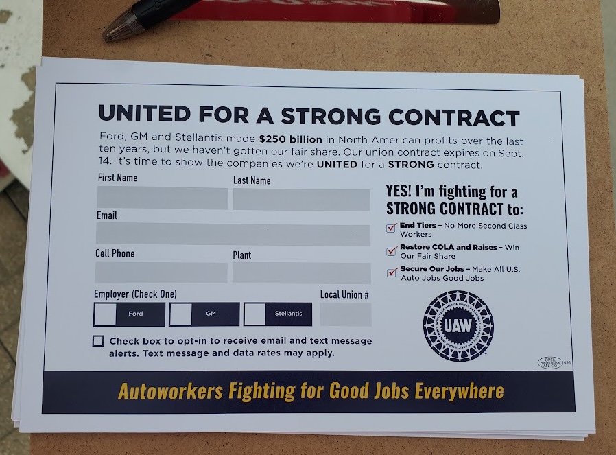 A piece of paper lies on a clipboard with a pen. The paper says ‘UNITED FOR A STRONG CONTRACT. Form, GM and Stellantis made $250 billion in North American profits over the last ten years, but we haven’t gotten our fair share. Our union contract expires on Sept. 14. It’s time to show the companies we’re UNITED for a STRONG contract.’ It has fields to be filled out, including NAME, EMAIL, CELL PHONE, and PLANT. It has the UAW wheel logo on it.